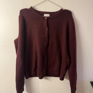 kofta - Mysig vinröd kofta med rund halsringning och knäppning framtill. Långärmad och i stickat material som känns både klassiskt och chill. Perfekt att slänga över en t-shirt eller ha som lager på lager under kallare dagar.