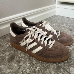 Adidas Spezial bruna sneakers mocka - Säljer ett par Adidas Spezial sneakers i brun mocka med vita detaljer och klassiska tre ränder på sidan. Helt nya, använda en gång, säljer då de inte passar mig, storlek 38. Ingår helt oanvända bruna snören samt skickas i adidas kartongen. Nypris 1349, mitt pris 1000kr