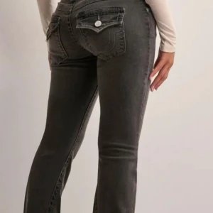 Grå low waisted bootcut jeans från true religion  - Säljer ett par grå jeans med bootcut-modell som är low waist och som har snygga fickdetaljer bak. Jeansen har en klassisk femficksdesign, silverfärgade knappar och är i stretchigt jeanstyg. Väldigt bra skick då dom bara använts fåtal gånger 