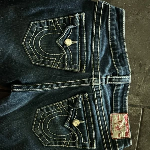 True Religion vintage jeans  - Snygga blå jeans från True Religion med tydliga kontrastsömmar och sjukt snygga fickor😍Inga defekter förekommer förutom att dragkedjan inte funkar🥲(kolla sista bilden) Säljer pågrund av att de är för små för mig!! Skriv om ni har frågor💕💕