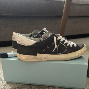 Philippe Model  - Säljer ett par mörkblåa Philippe Model sneakers i skinn med vita detaljer och vit sula. Skorna har storlek 43 och har en klassisk snörning, rund tå och en ikonisk sköld på sidan. Insidan är ljus. Extra skosnören i mörkblått medföljer. Även lådan med skorna. Knappt några defekter bara att höra av sig!