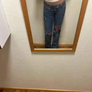 Blå slitna jeans med hål på knäna - Säljer ett par blå jeans med raka ben och stora slitningar över båda knäna. Byxorna är från lager men hålen är gjorda själv