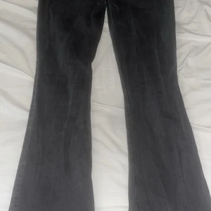 Svarta bootcut jeans från Lager 157 - Säljer ett par svarta bootcut jeans från Lager 157 i storlek S. Jeansen har full längd och är tillverkade i klassiskt denimtyg. De har en snygg utsvängd passform nertill och råa, slitna detaljer vid benslutet för en cool look. Lite trasiga längst ned på ena sidan. 