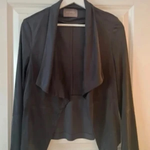 Jacka - Säljer en svart jacka från Orsay med omlottkrage och lång ärm. Jackan har en öppen front och en elegant, draperad passform. Perfekt för att lyfta en enkel outfit.