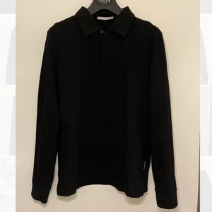 Tiger of Sweden piké med unik krage - Svart långärmad piké från Tiger of Sweden. Kragen ”knäpps” med en unik snörloop som gör att den alltid hålls snyggt öppen. Säljs endast för att den är för liten för mig, tycker den är skitsnygg. Endast använd en gång. Frakt tillkommer.