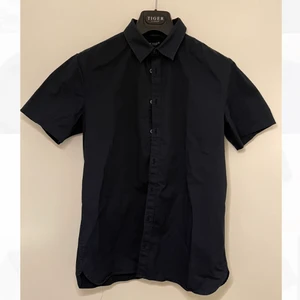 Kortärmad blank skjorta Tiger of Sweden - Kortärmad mörkblå skjorta från Tiger of Sweden i blankt material. Luftig och skön för sommaren och sitter snyggt med bra struktur. Kragstorlek 40 vilket motsvarar medium. Frakt tillkommer. 