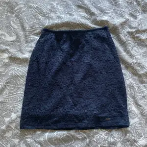 Kort, tight, mörkblå kjol med spetsmönster från Hollister.
