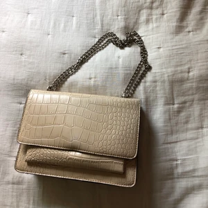 Beige väska med kedjeband  - Köpt från Nelly för något år sedan och inte använd på länge! Beige i fake-skinn med silverkedjor och har två olika fack, och den är rymlig! Perfekta vardagsväskan🥰