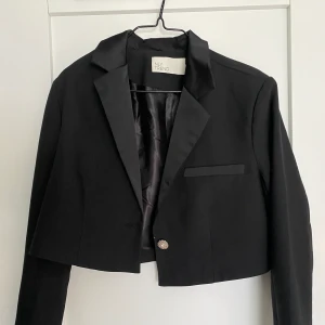 Kort kavaj  - En kavaj i kort modell. Skitsnygg till kjol eller högmidjade kostymbyxor! Säljer pga får ej tillfälle att använda den. Använd endast en gång🖤 jättefint kostym material, köpt från Nelly. 