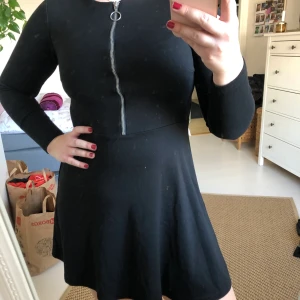 Svart klänning med dragkedja - Svart klänning från Vila i stl S! Klänningen är i stretchigt tyg med en dragkedja framtill som går att stänga hur man vill. Klänningen är använd ett fåtal gånger och är i bra skick för att den har väldigt bra kvalite. 