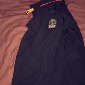 Parajumpers vindjacka - Parajumpers vindjacka i använt skick, finns ett hål cirka en tumnagel stort men syns ej när man har den på sig då kragen ”viker” sig över! Finns även luva man kan fälla ut/fälla in.
