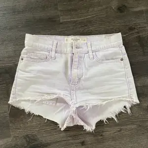 Ett par korta jeans shorts i färgen vit med en lila nyans på vissa ställen. 