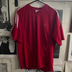 Röd adidas t-shirt. Adidas-ränder längs axlarna. Något urtvättat adidas-märke på framsidan  