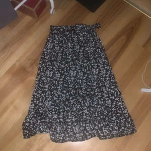 Kjol blommig - Supersöt blommig kjol med en liten knutdetalj uppe vid midjan! Volanger nedtill, blir lite längre där bak än där fram. Går ner till mitt på smalbenen på mig. Sitter tajt runt midjan. Inte stretchig. Den har därför en liten dragkedja under rosetten.