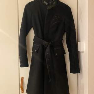 Höst/vinterkappa i svart med dragkedja och skärp. Firgurnära modell.
