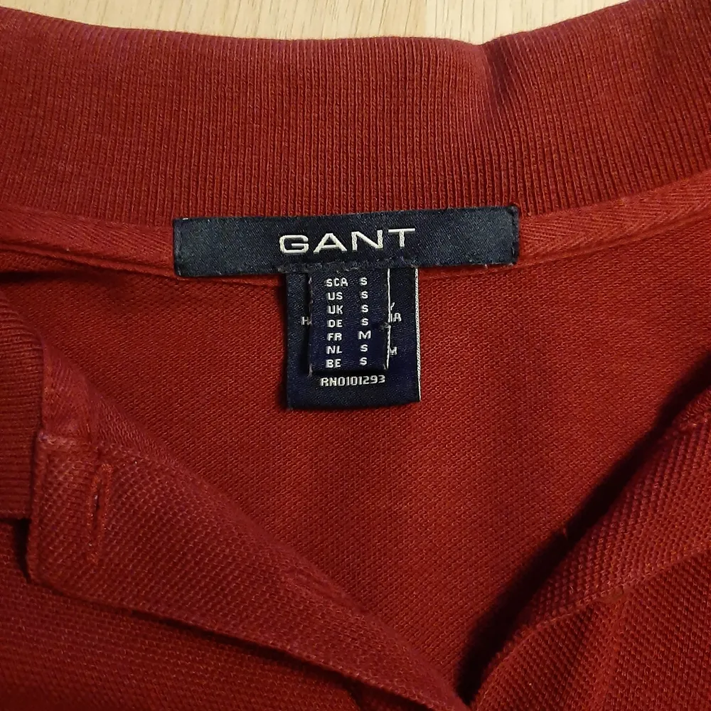 En röd gant poloskjorta i dam modell. Tyget är lite tjockare än vanligt skjort typ. Den har fyra knappar som man kan ha uppknäppta eller inte. Storlek S men passar även som M. (Har vikt upp den). Skjortor.
