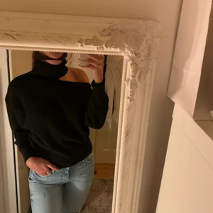 Stickad tröja med hög hals - Svart stickad tröja med hög hals och öppen vid ena axeln. Helt ny med prislapp kvar.