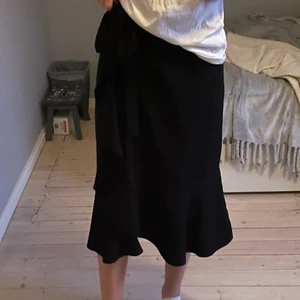 Svart kjol - En knälång svart kjol i storlek 36 från Gina tricot. Man kan knyta kjolen lösare eller hårdare vilket innebär att den passar flera storlekar. Den är tunn och fladdrig med volanger längst ner. Den är använd ca 3 gånger så de. Är i väldigt gott skick! Passar alla längder beroende på hur lång man vill att den ska vara!