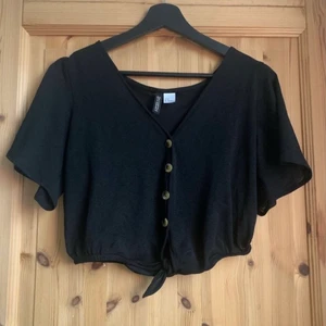 Svart topp/blus - Detta är en topp/blus som är väldigt pösig i materialet. Den har knappar på framsidan samt en knytning längst när och är lite kroppad i designen.  Toppen/blusen kommer från HM och har använts 2/3 gånger men är annars i väldigt gott skick🤍 