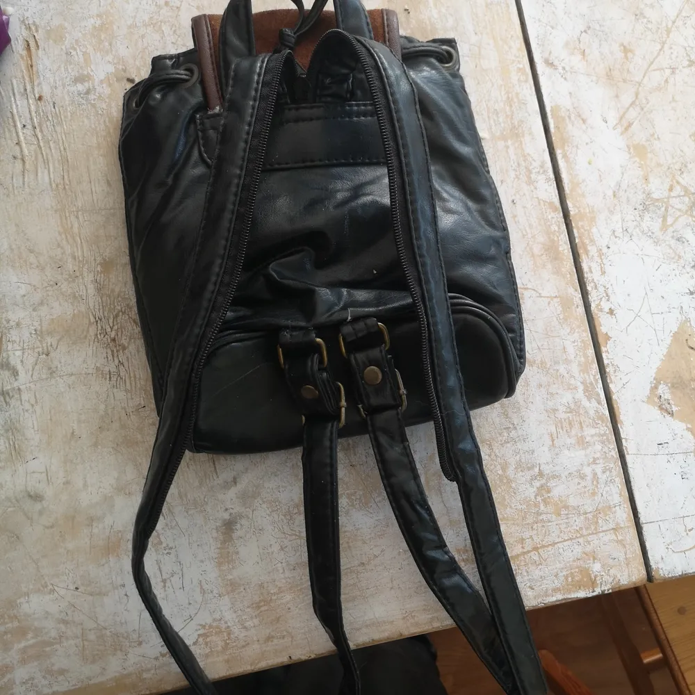 Liten svart läder ryggsäck med brun mocka detalj. Väskor.