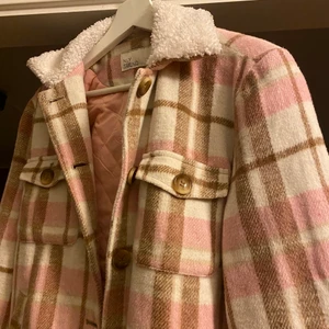 Rutig jacka - Rutig jacka från Nelly i rosa, vit och brun med fluffig krage. Säljer då jag tror att den kommer komma till mer användning hos någon annan💞 skriv vid frågor🥰