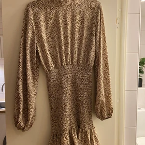 Beige/brun klänning - Säljer denna fina klänning med ballongarmar och resår runt midjan/rumpan och volang ner till. Passar bra i längd på mig som är 165 cm🤎 storlek M