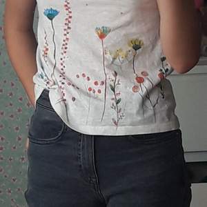 Vit T-shirt med färgglatt blommtryck på framsidan och lite paljetter/glitter. Baksidan är dekorerad med en 