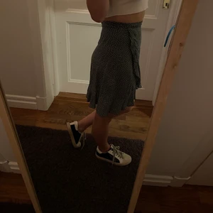 Grön, prickig kjol - Endast använd en gång, som ny. Går att knyta på olika sätt (volangen kan både sitta på sidan samt framtill beroende på hur man knyter) jättefin med strumpbyxor och en tjocktröja nu till hösten! Obs, kjolen är inte jättelång, det är endast jag som har korta ben!