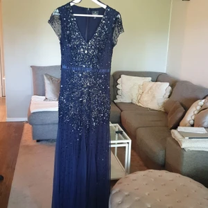 Mörkblå maxi klänning - Mörkblå aftonklänning med vackra detaljer. V-ringad framtill, dragkedja baktill. Broderade stenar och paljetter. Använd endast en gång. Saknas någon sten eller paljett på enstaka ställen på klänningen, men det är ingenting man riktigt lägger märke till. Storlek: 38. Märke: ADRIANNA PAPELL, köpt utomlands.