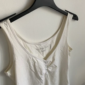 Enkelt vitt linne  - Vitt linne med två knappar i bysten. 95 % bomull. 