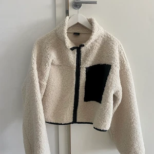 Teddy vårjacka  - En off-white Teddy jacka ifrån Gina, svarta detaljer och stor bröstficka. Hög krage och cropad i längden. Passformen är bred och oversized så passar många. Storlek M. På den tunnare sidan, perfekt till våren. Mycket bra skick