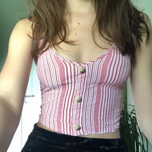 Randig croptop med knappar - Gullig croptop med röd-vit randigt mönster. Stretchig där bak så den sitter inte för tajt utan passar perfekt, axelbanden kan också justeras. Bästa sommarplagget men passar också under en mysig kofta på vintern