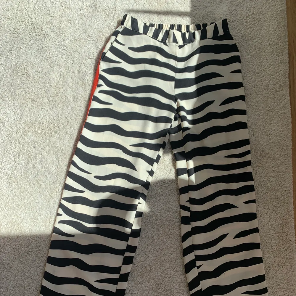 Slutsålda byxor från Lindex. Byxorna är i zebra tyg med en orange/röd detalj längs båda sidorna. Storlek XS. Jag är 162 lång och byxorna passar mig perfekt i längden. . Jeans & Byxor.
