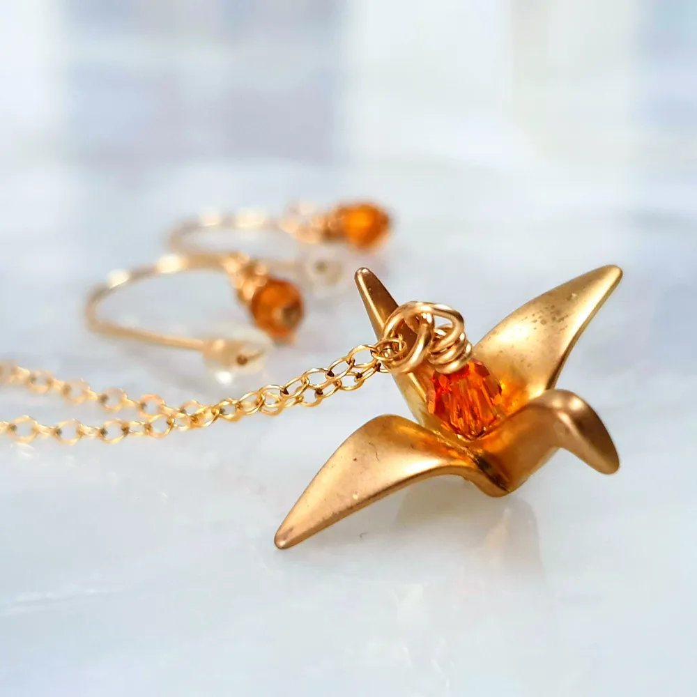 Guld färgad origami fågel halsband med tillhörande örhängen. Otroligt fint halsband med orangea glas pärlor som reflekterar ljuset så att det ser ut som att dem lyser. Kontakta vid intresse😇🐦. Accessoarer.