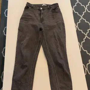 Ett par mörk gråa jeans som är insydda i midjan för en bättre passform, detta syns inte på utsidan 