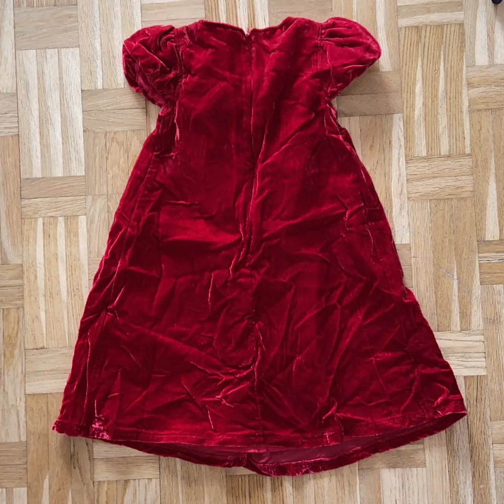 Röd klänning med en liten rosett, för barn. Jag hittar ingen storlek men hade själv på mig den som 4 åring, funkar säkert på 3-5 år.. Klänningar.