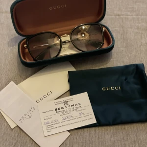 Gucci solglasögon  - Säljer Gucci solglasögon då dom tyvärr är lite förstora. Inköpta 2020, men bara använda 2-3 gånger. Äkthets bevis finns, modell 0606SK i färg 001 (svart/guld) storlek 56-19. Nypris 3850kr, Oanvänd putsduk samt fodral/siden påse medföljer 