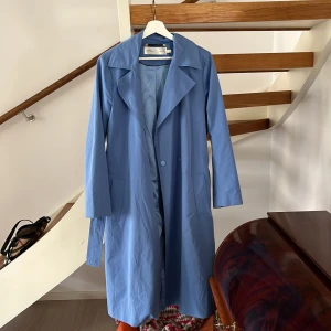 Trenchcoat  - Blå trenchcoat från InWear Copenhagen. Extremt skönt material både inuti och utanpå. Går nedanför knävecken på mig. Bälte tillhör