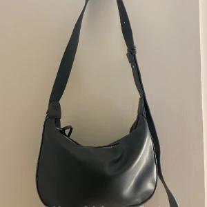 Väska - Väska i en blåaktig färg. Aldrig använd. Går att justera och ha både som crossbodybag och shoulderbag