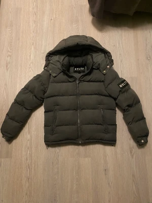 Grå Nvlty Jacka - Jag säljer denna riktigt snygga gråa Nvlty jacka, väldigt varm och passar perfekt till vintern. Den är i nyskick och ser ut som helt ny, bara använd i ungefär en månad. Luvan är också avtagbar. Unik eftersom inte många i Sverige ha börjat använda Nvlty.