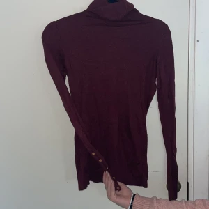 Vinröd polo - En polo med fina guldknappar på armarna.