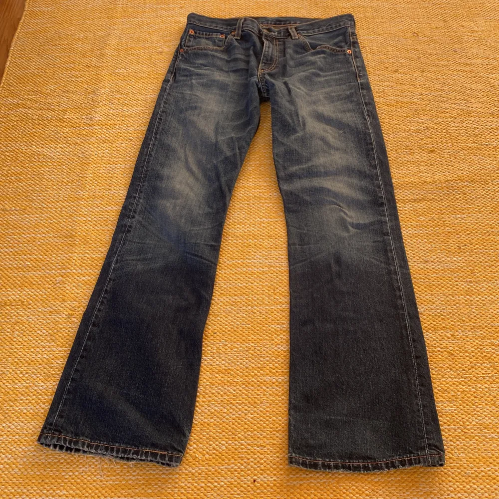 Mörkblåa Levi’s Jeans med ljupa fickor fram. Lite bootcut modell, sitter bra runt låren och lite lösare längre ner på benet. Slitna nere vid kanten.. Jeans & Byxor.