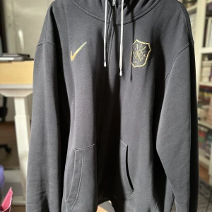 AIK NIKE Zip-Hoodie - Oanvänd svart AIK zip-hoodie från Nike med klubbens första emblem och logotyp i guld. Begränsad upplaga. Säljes pga platsbrist