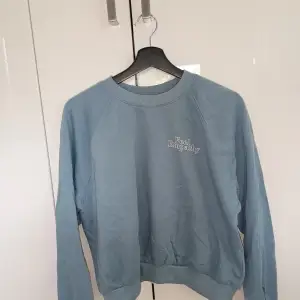 En ljusblå sweatshirt i storlek M. Med texten 