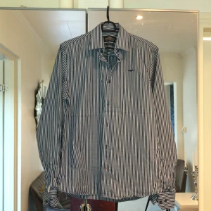 Skjorta  - Marinblå och vit randig skjorta, perfekt till sommaren och vid tillställningar. 