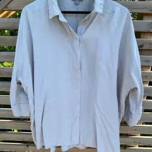 Ljusgrå skjorta i lyocell från Cos. Avslappnad modell, något längre baktill. Trekvartärm. Mycket gott skick. 
