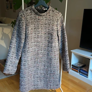 Business-klänning - Stilren och smickrande klänning i grövre tyg med glittriga inslag. Använd ett fåtal gånger. Fodrad och med snyggt fall. Passar dig som har stl 36. Längd på hela klänningen är 87 cm. 