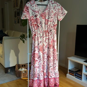 Romantisk maxiklänning - Fin maxiklänning med kort ärm och v-ringad hals, svalt men inte genomskinligt material, längd 130 cm, resår i midjan. Volang längst ned