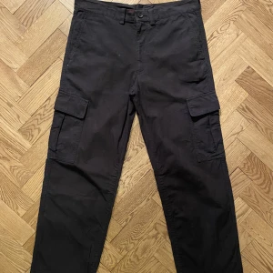 Issey Miyake Cargobyxor - Ett par enkla cargobyxor från japanska designern Issey Miyake. Har en mörk mörkblå färg. Ganska basic men är gjort av skönt material och är kvalle.!Har en liten missfärgning vid knappen på framsidan. Annars bra.  Storlek 3-4, sitter som en 34/32 ungefär. 
