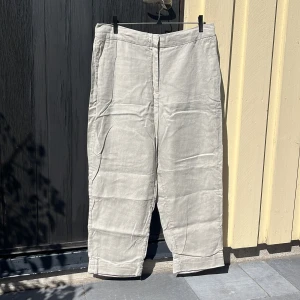 Beiga linnebyxor - Ett par somriga beiga linnebyxor. Har två djupa framfickor och två byxkrokar samt dragkedja som stängning. 100% linne 